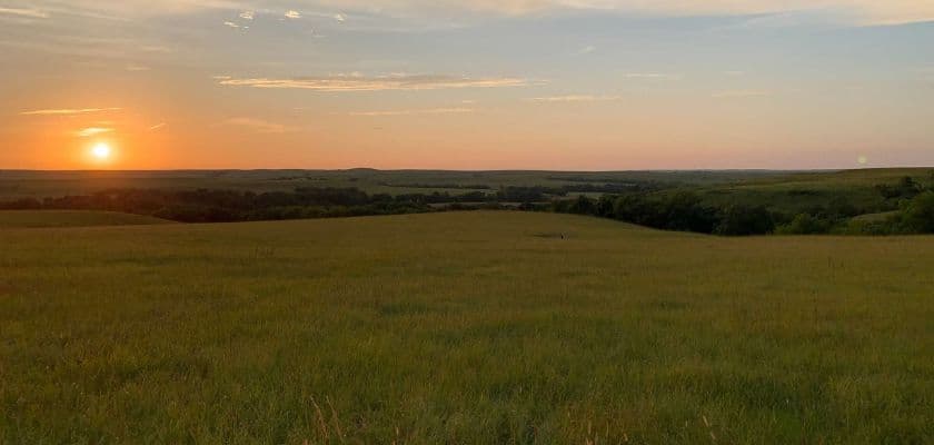 A serene landscape at sunset, showcasing rolling hills and a vibrant sky.