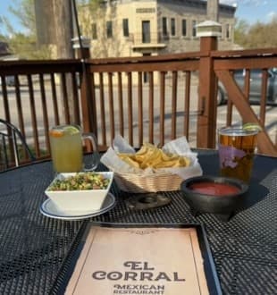 A table at El Corral restaurant featuring chips, salsa, a salad, drinks, and a menu.