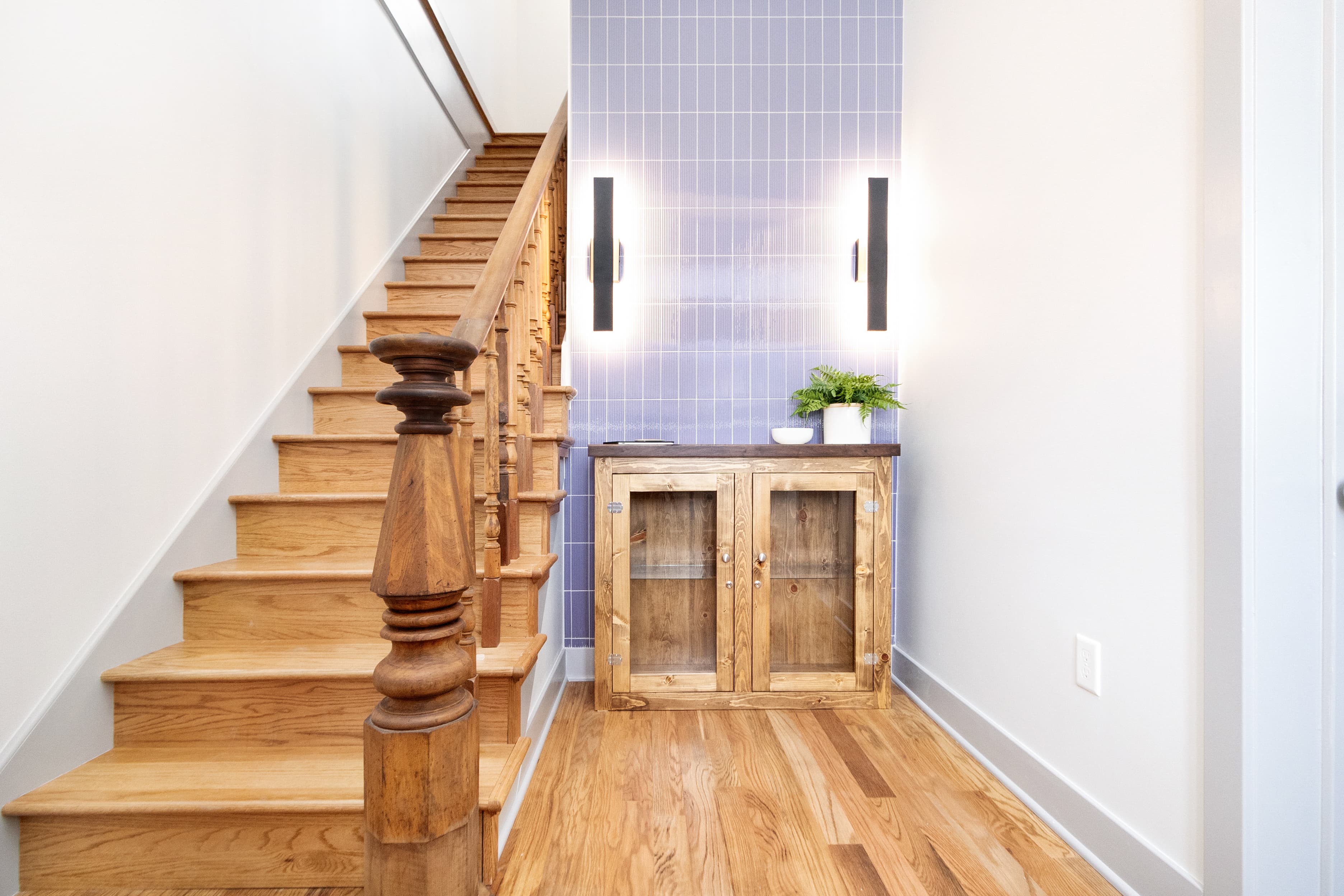 A wooden staircase leads up to a hallway with a blue tiled wall and a wooden console table adorned with a small plant.