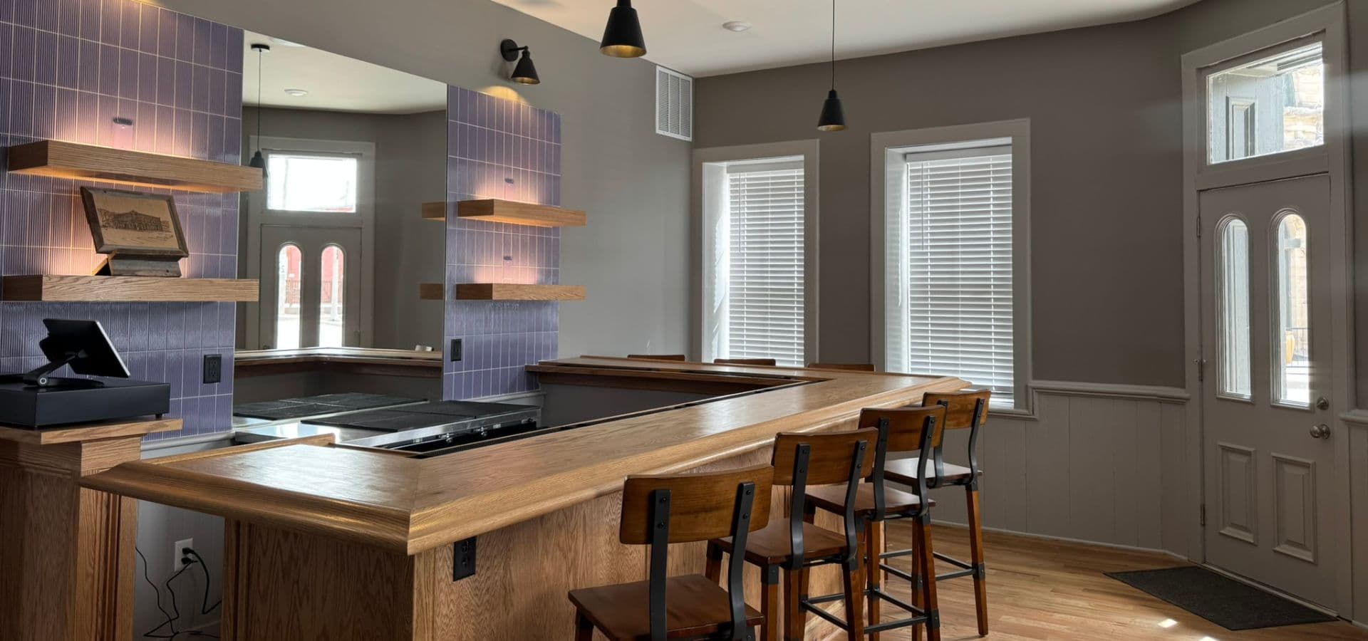 Modern kitchen interior featuring a wooden bar, stools, and purple tile accents.