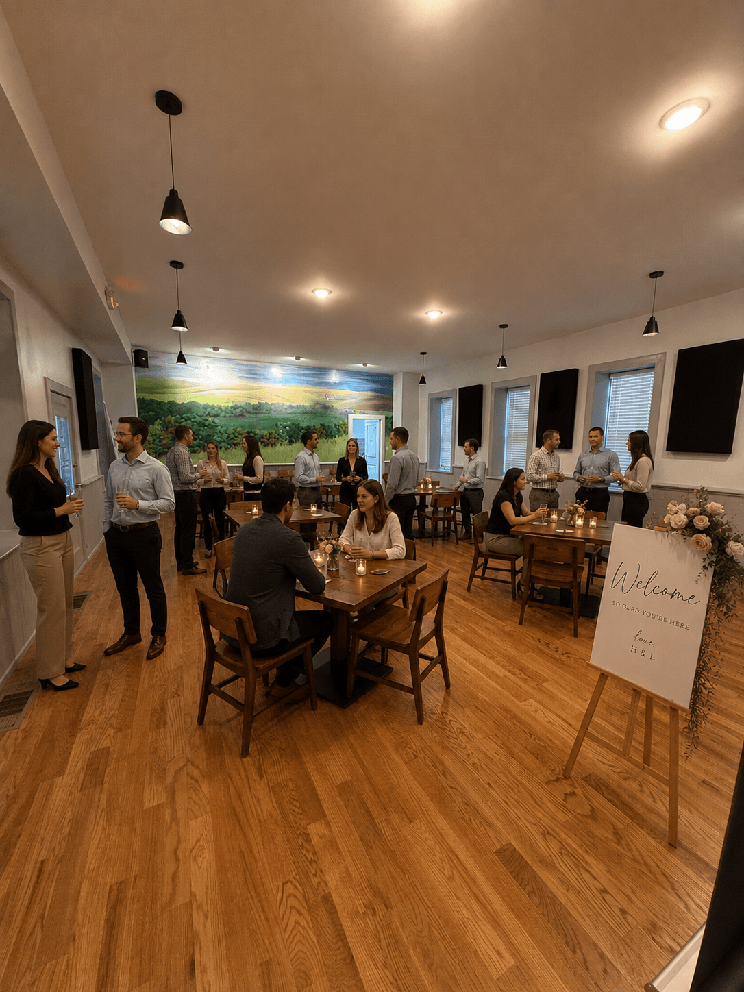 A social gathering in a warmly lit room with people conversing and a "Welcome" sign on display.