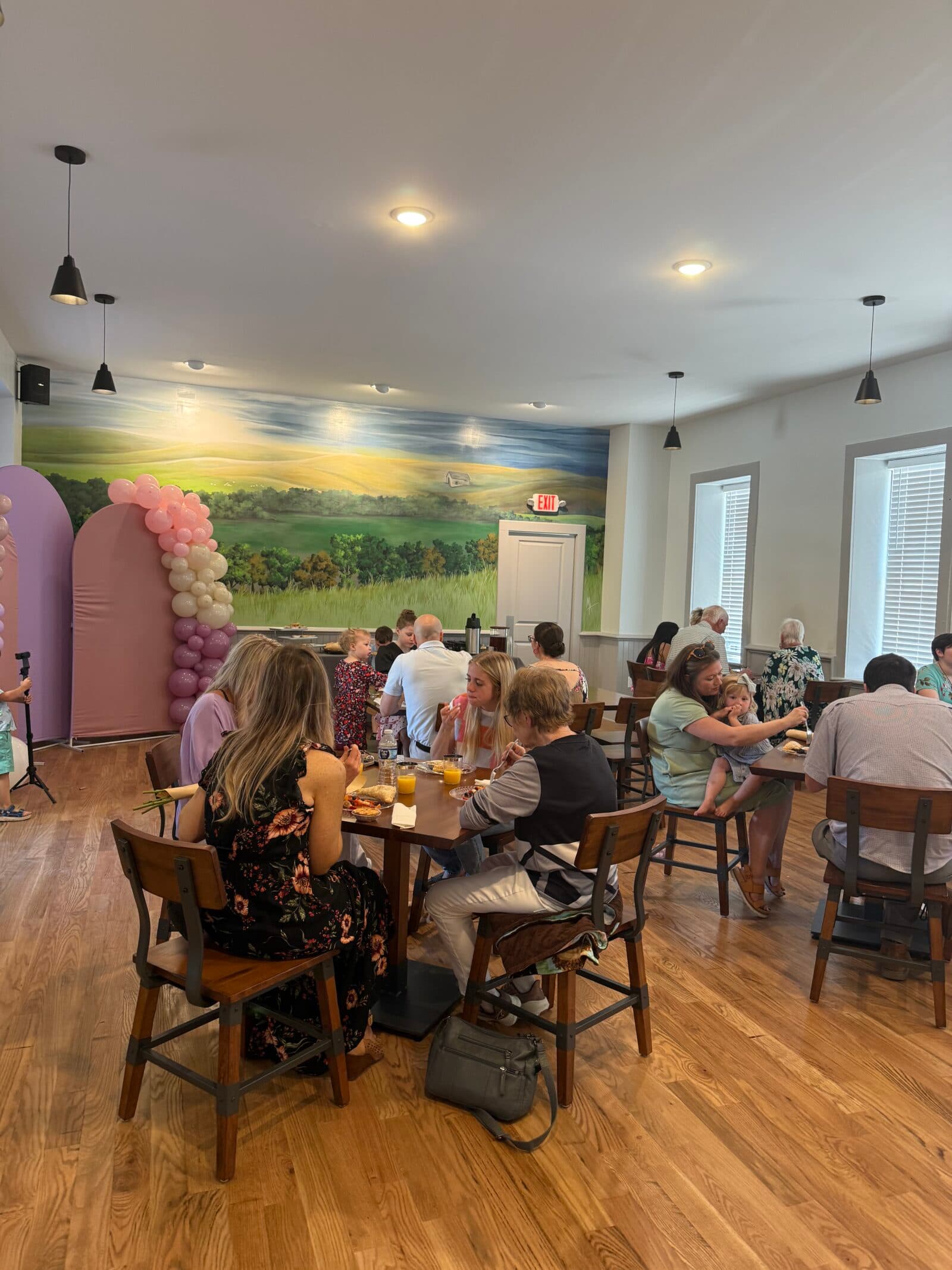 A cozy restaurant setting with guests dining and a colorful balloon arch in the background.