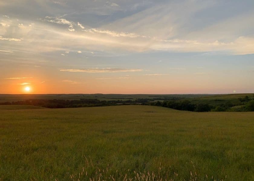 A serene landscape at sunset with rolling hills and an expansive sky.