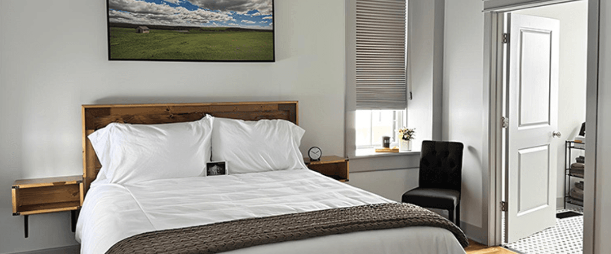 A modern bedroom with a neatly made bed, featuring a wooden headboard and a chair beside a window.