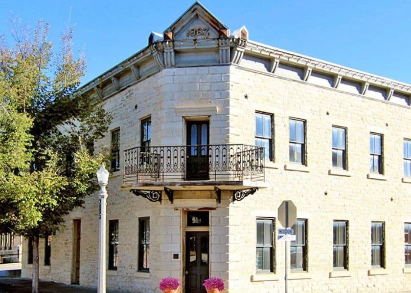 Historic stone building with a decorative balcony and surrounding trees.