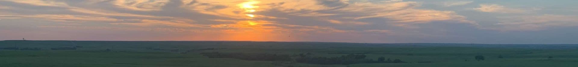A panoramic view of a sunset over lush green fields and a colorful sky.