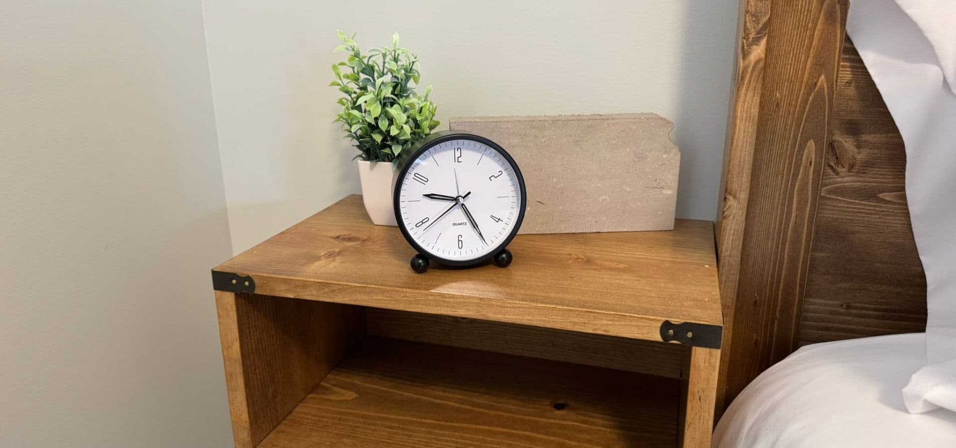 A wooden nightstand with a clock and a small potted plant.