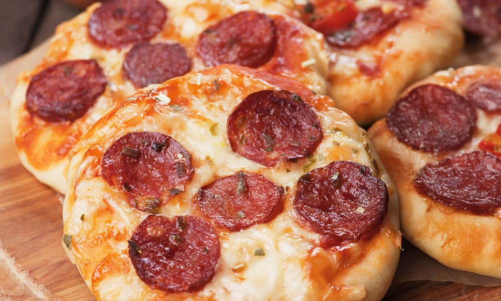 Four mini pepperoni pizzas on a wooden board.