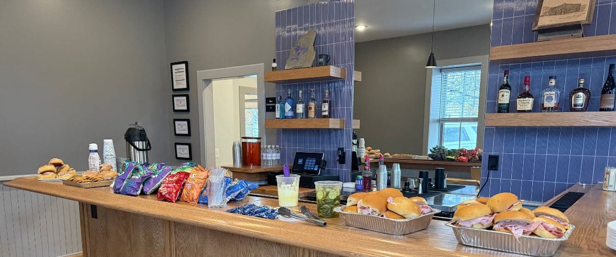 A countertop displays an assortment of sandwiches, snacks, and beverages in a cozy setting.