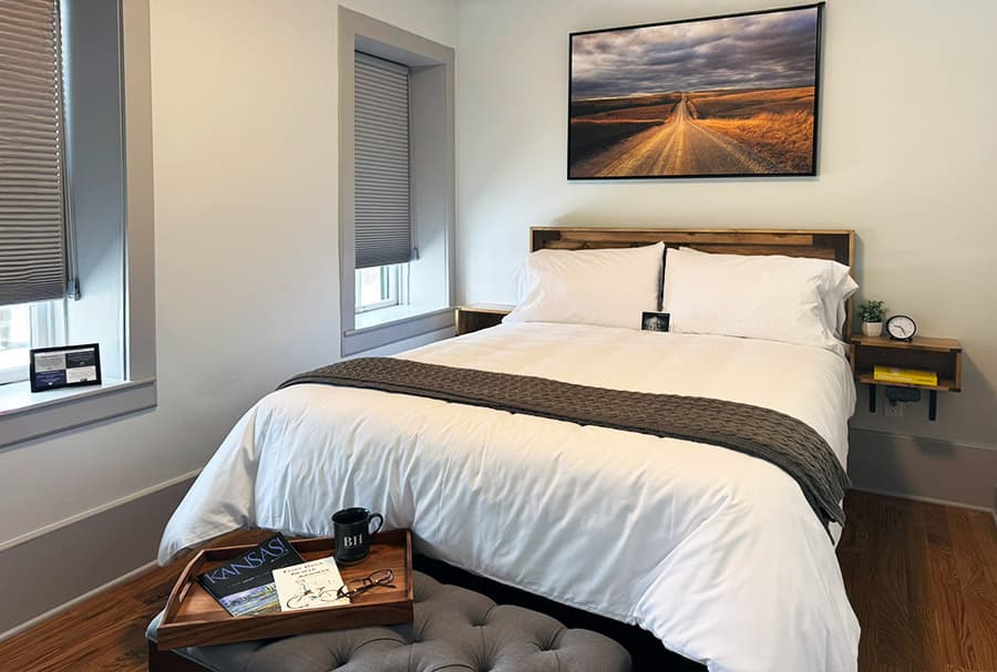 A cozy bedroom featuring a queen-sized bed, decorative artwork, and a small side table with personal items.