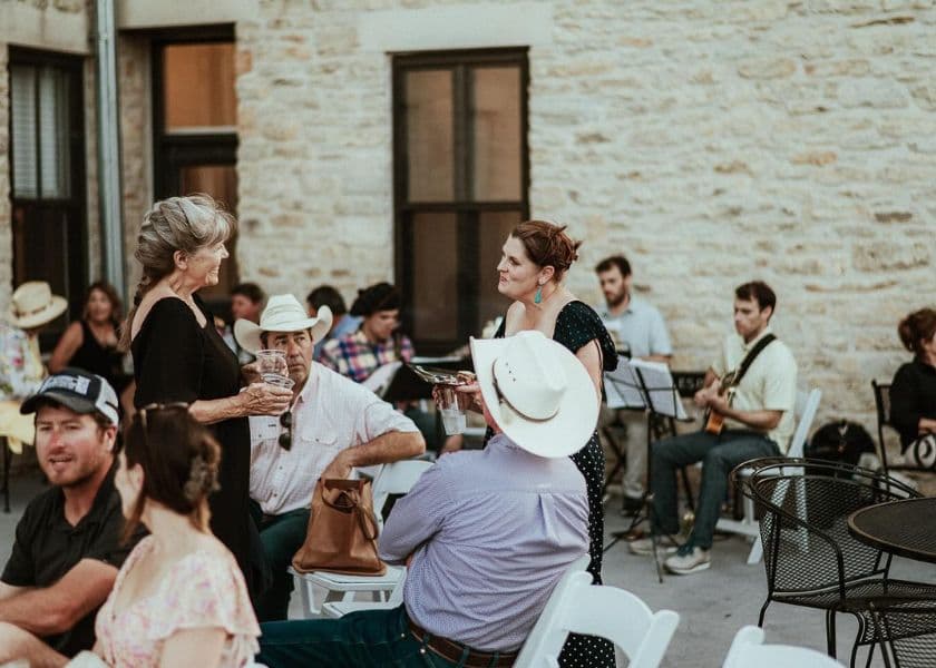 A group of people socializes outdoors at a gathering, with a band playing in the background.