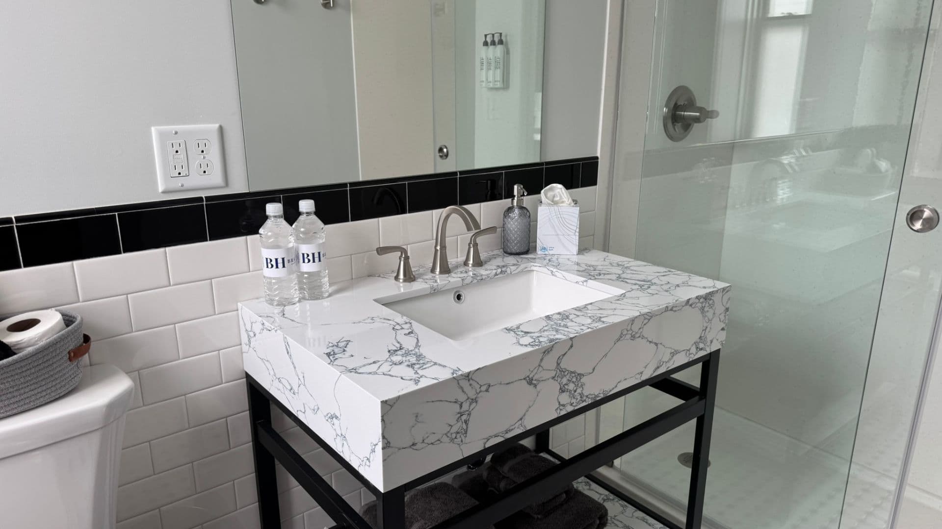 A modern bathroom vanity with a marble countertop, sink, and two water bottles.