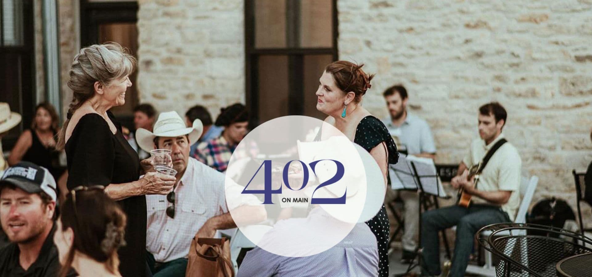 A lively outdoor gathering at 402 on Main, featuring people socializing and a live band in the background.