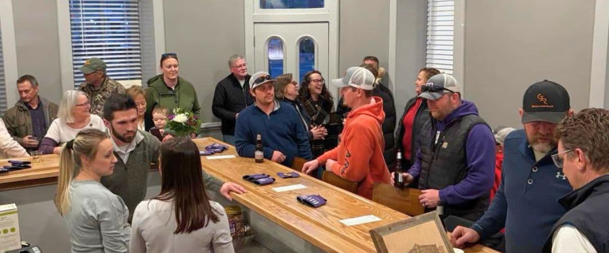 A lively crowd gathers at a bar with a wooden counter, chatting and enjoying drinks.