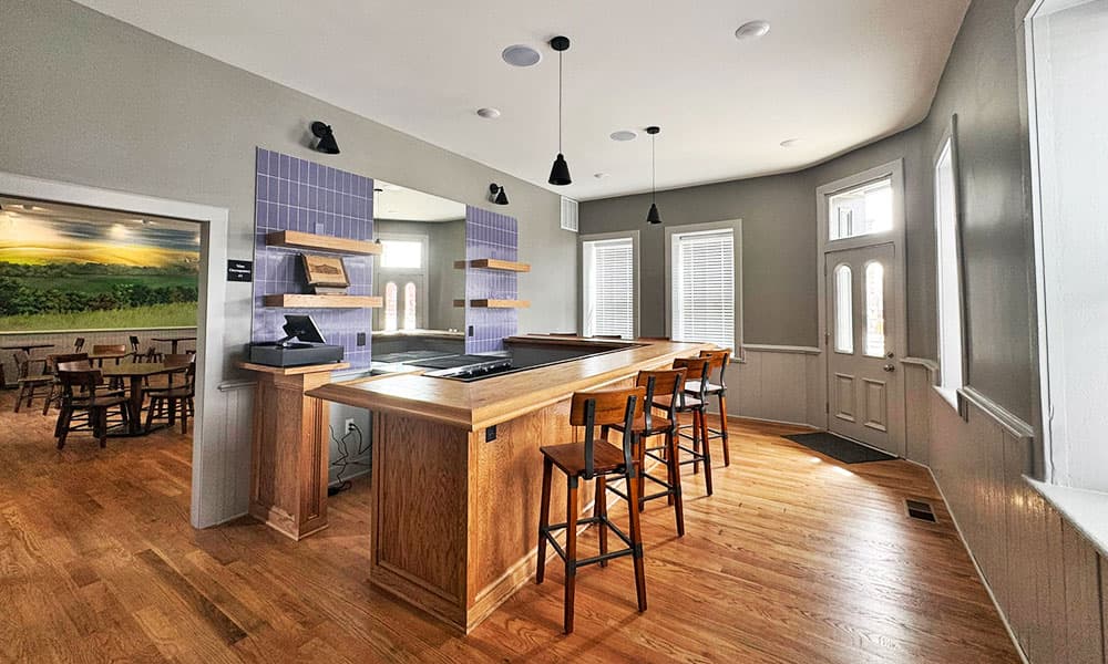 A modern kitchen with wooden flooring, a large island bar, and seating, featuring natural light from multiple windows.