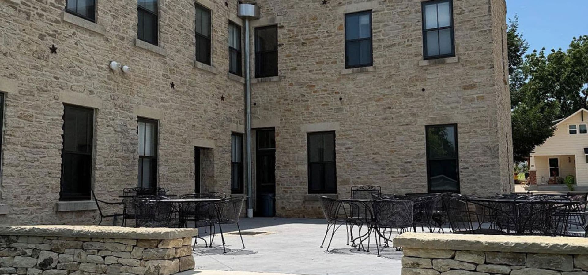 A stone-walled courtyard outside a building with several tables and chairs.