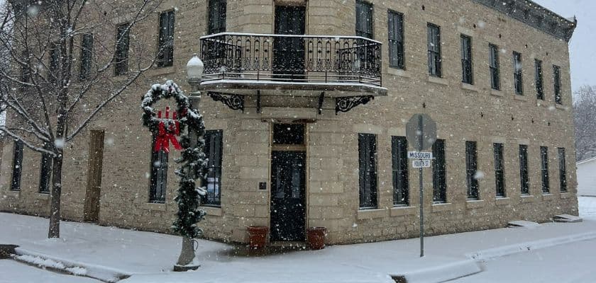 Historic stone building adorned with a holiday wreath, surrounded by falling snow.
