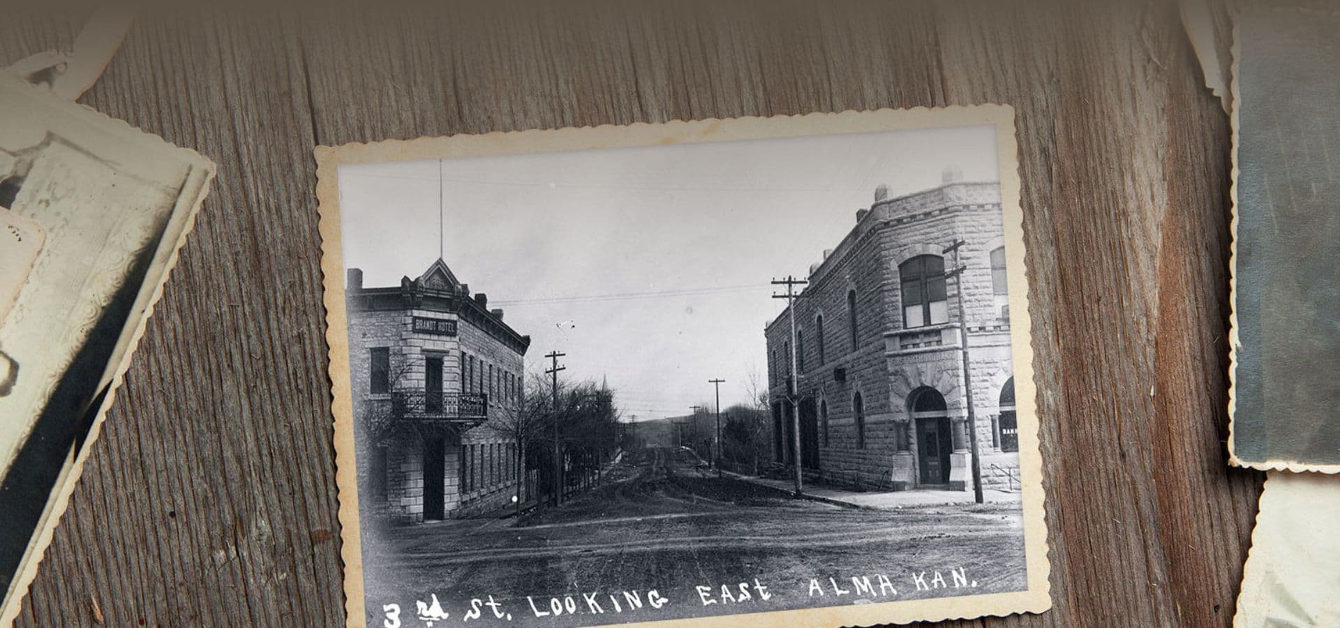 Black-and-white photograph of 3rd Street in Alma, Kansas, looking east, featuring historic buildings and telephone poles.