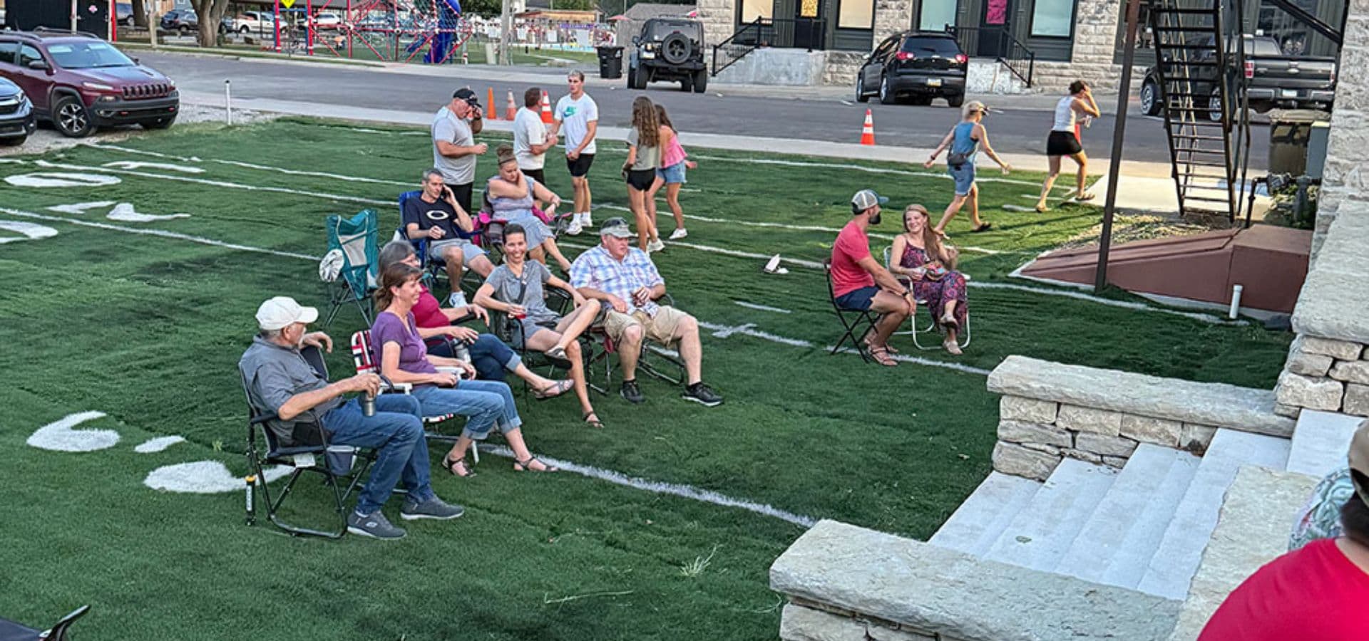 A group of people sitting on a grassy area watching an event, with some also walking around in the background.
