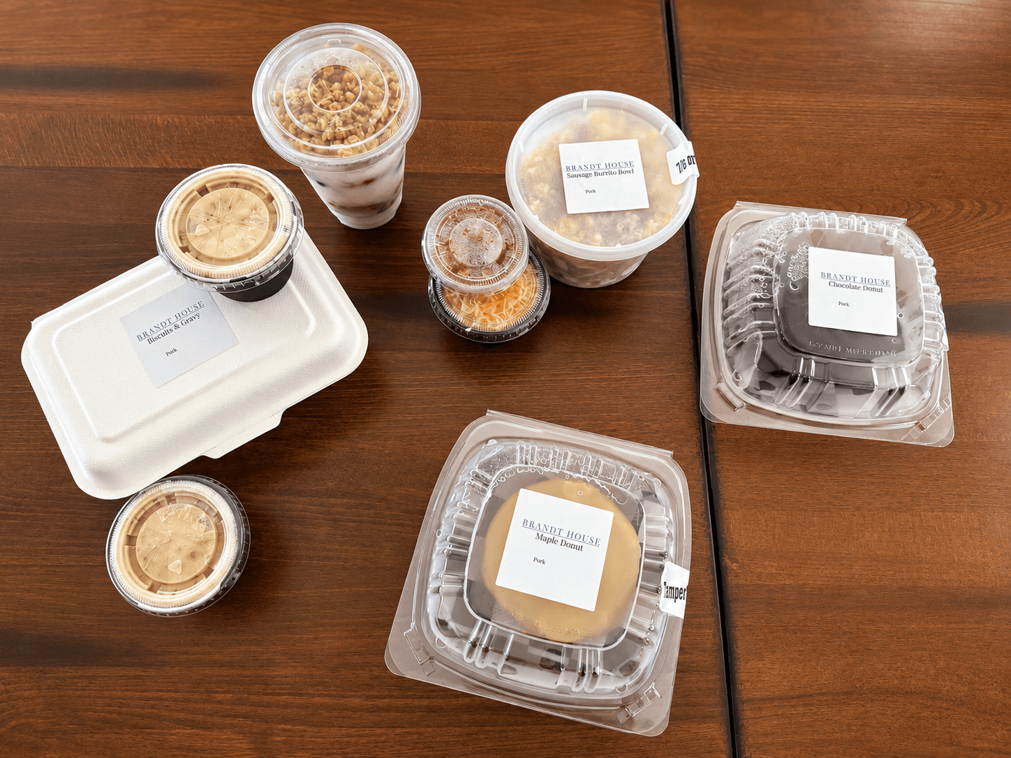 A collection of takeout containers and beverages from a restaurant arranged on a wooden table.