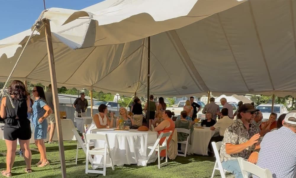 A lively gathering of people enjoying a meal under a large tent.